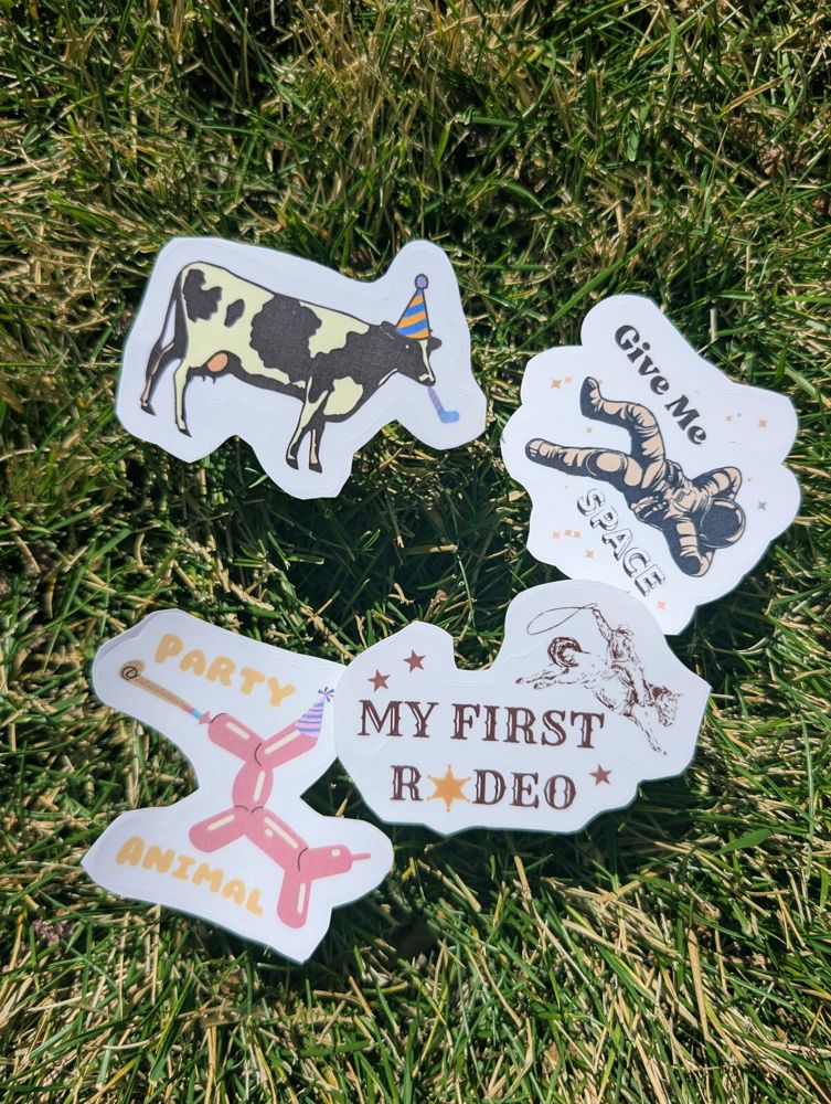 Four die-cut party stickers on grass: a cow in a party hat, Give Me Space, Party Animal and My First Rodeo